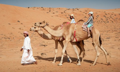 Beduine führt zwei Kamele mit zwei Mädchen durch die Wüste – Oman Familienreise