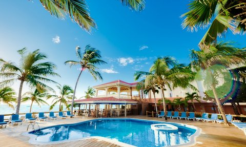 Ein einladender Poolbereich umgeben von Palmen, mit einem klaren blauen Himmel und einem charmanten Hotel im Hintergrund.