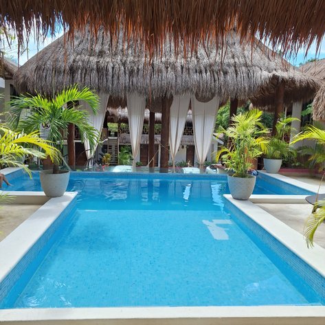 Ein einladender Poolbereich mit klarem Wasser, umgeben von tropischen Pflanzen und einem strohgedeckten Dach.