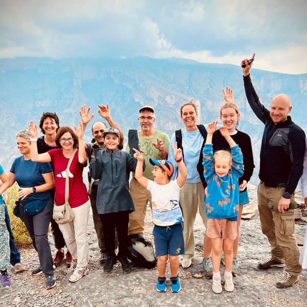 Reisegruppe posiert gemeinsam mit ihrem Guide vor der Bergkulisse des Jebel Shams – Oman Reise mit Kindern