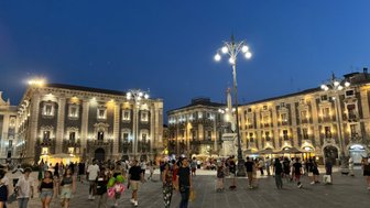 Die belebte Piazza Duomo in Catania ist bei Nacht erleuchtet, mit Menschen, die fröhlich umhergehen und die Atmosphäre genießen.