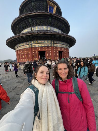 Zwei Frauen posieren lächelnd vor dem beeindruckenden Himmelstempel in Peking, umgeben von einer großen Menschenmenge.