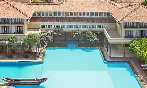 Ein weitläufiger Pool umgeben von tropischen Pflanzen und einem eleganten Gebäude mit traditioneller Architektur.