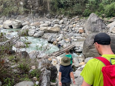 Eine Gruppe von Wanderern geht einen steinigen Pfad entlang, umgeben von üppiger Natur und einem rauschenden Fluss.