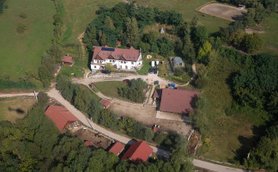 Eine Luftaufnahme zeigt ein weitläufiges Gelände mit einem großen, weißen Gebäude und mehreren roten Dächern in der Umgebung.