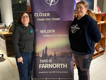 Zwei Frauen stehen lächelnd neben einem Banner von Tailored Adventures, das die Schönheit des Nordens bewirbt.