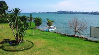 Ein ruhiger Blick auf den Viktoriasee, umgeben von üppigem Grün und Palmen, mit einem Boot, das am Ufer anlegt.