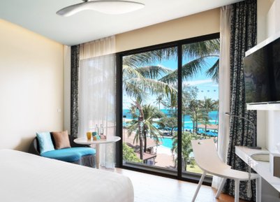 Ein modernes Hotelzimmer mit Blick auf einen Pool und Palmen, das eine entspannende Atmosphäre ausstrahlt.