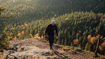 Ein Wanderer erklimmt einen felsigen Hang, umgeben von einer atemberaubenden Waldlandschaft im goldenen Licht der Abenddämmerung.