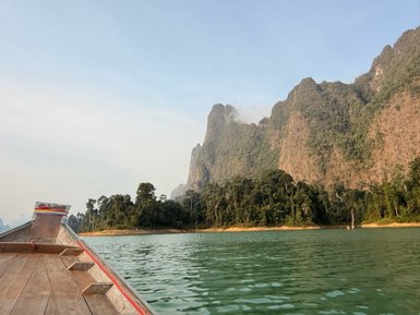 Ein Longtailboot gleitet über das ruhige Wasser, umgeben von majestätischen Bergen und üppigem Grün im Khao Sok Nationalpark.