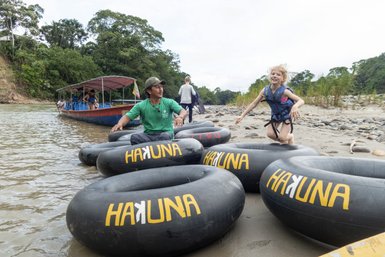 Ein fröhliches Kind springt auf einem Sandstrand, umgeben von Reifen mit der Aufschrift 'HAKUNA'.