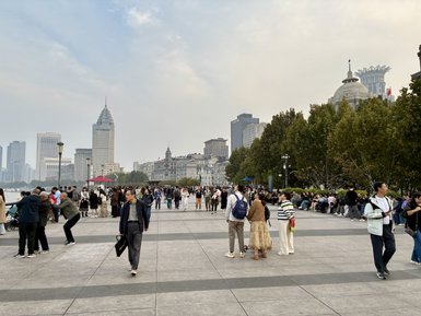Eine belebte Promenade in Shanghai, gesäumt von Menschen, die die Aussicht auf die Stadt und den Fluss genießen.
