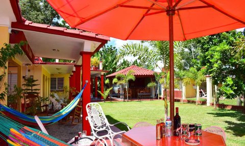Ein einladender Gemeinschaftsbereich mit bunten Hängematten und einem großen roten Sonnenschirm, umgeben von üppigem Grün.