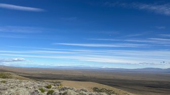 Eine weite, offene Landschaft in Patagonien, mit sanften Hügeln und einem strahlend blauen Himmel voller Wolken.