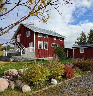 Ein rotes Holzhaus mit einem modernen Design steht in einer grünen Umgebung, umgeben von bunten Pflanzen und Steinen.