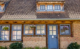 Die Fassade eines charmanten Hauses mit blauen Fenstern und einer blauen Tür, umgeben von bunten Blumen und Pflanzen.
