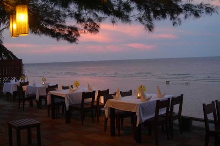 Ein romantisches Restaurant am Strand mit Tischen, die für ein Abendessen bei Sonnenuntergang gedeckt sind.