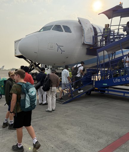 Eine Gruppe von Passagieren steigt an einem Flughafen in ein Flugzeug ein, während die Sonne am Horizont untergeht.