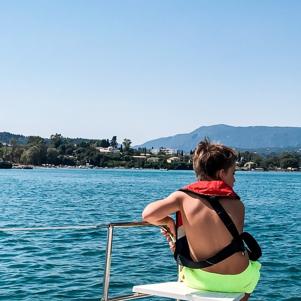 Zwei Kinder in Schwimmwesten genießen die Aussicht auf das Wasser und die umliegenden Berge an einem sonnigen Tag.