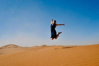 Frau beim Springen in den Sanddünen der marokkanischen Wüste – Familienurlaub in Marokko