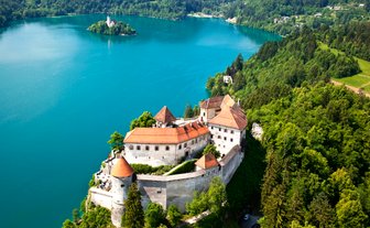 Eine atemberaubende Aussicht auf die Burg Bled, umgeben von üppigem Grün und dem glitzernden Wasser des Sees.