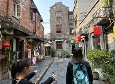 Eine Frau mit einem Rucksack steht in einer schmalen Gasse, umgeben von historischen Backsteingebäuden und roten Laternen.