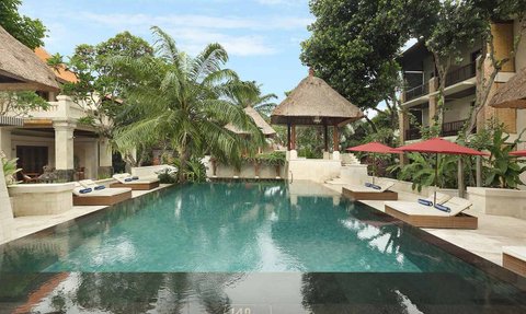 Ein ruhiger Poolbereich in Bali, umgeben von tropischen Pflanzen und Sonnenliegen unter roten Sonnenschirmen.