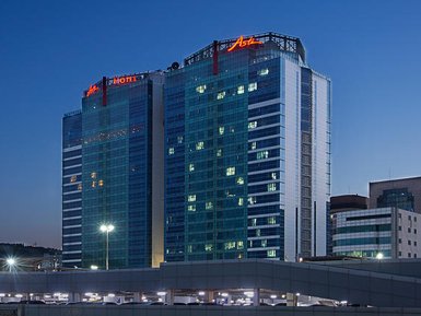 Das Asti Hotel in Busan erstrahlt in der Dämmerung, mit leuchtenden Fenstern und einem modernen Glasdesign.