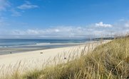 Ein weitläufiger Strand mit feinem Sand erstreckt sich unter einem strahlend blauen Himmel und sanften Wellen.