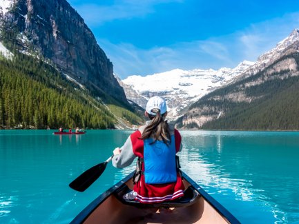 Eine Person paddelt in einem Kanu auf dem türkisfarbenen Wasser des Lake Louise, umgeben von majestätischen Bergen.