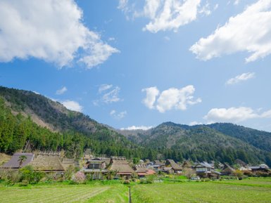 Eine malerische Landschaft mit traditionellen japanischen Häusern, umgeben von grünen Bergen und einem strahlend blauen Himmel.