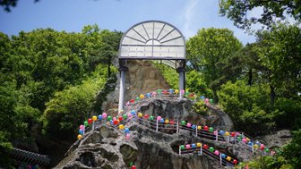 Eine bunte Treppe aus Ballons führt zu einer beeindruckenden Felsformation, die von üppigem Grün umgeben ist.
