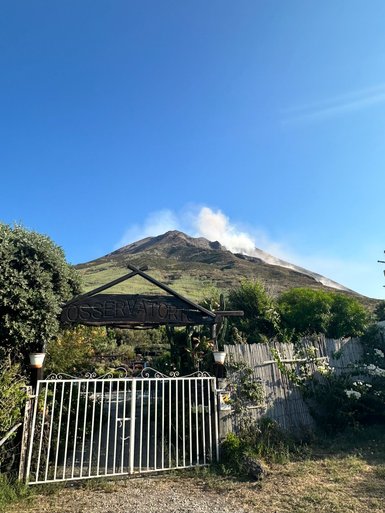 Der Blick auf den Stromboli zeigt einen rauchenden Vulkan unter einem strahlend blauen Himmel, umgeben von üppiger Vegetation.