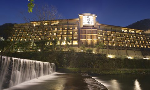 Ein elegantes Onsen-Hotel in Hakone, beleuchtet bei Nacht, mit einem sanften Wasserfall im Vordergrund.