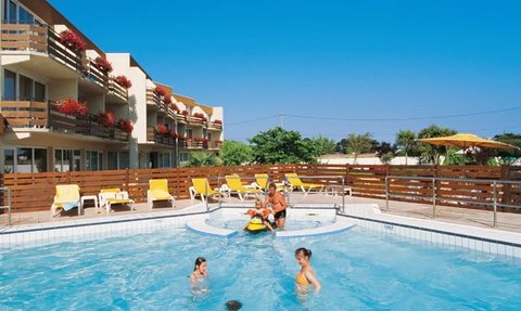 Ein sonniger Poolbereich mit fröhlichen Kindern, die im Wasser spielen, umgeben von Liegen und blühenden Pflanzen.