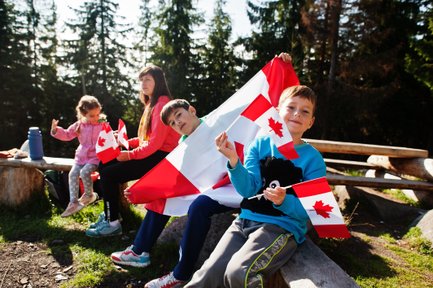 Eine Gruppe von Kindern sitzt im Freien und hält kanadische Flaggen, während sie fröhlich in die Kamera lächeln.