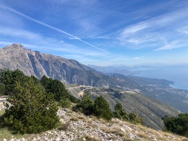 Ein atemberaubender Blick auf die Berge und das Meer, umgeben von üppigem Grün und klarem, blauem Himmel.