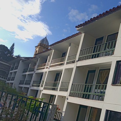 Ein modernes Hotelgebäude mit mehreren Etagen, umgeben von üppigem Grün und einem klaren blauen Himmel.