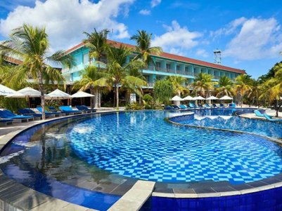 Ein luxuriöser Pool mit blauen Fliesen, umgeben von Palmen und Liegen, unter einem strahlend blauen Himmel.