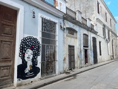 Eine Wandmalerei zeigt einen Sänger mit Afrofrisur, der ein Mikrofon hält, vor einer alten, blauen Hausfassade.