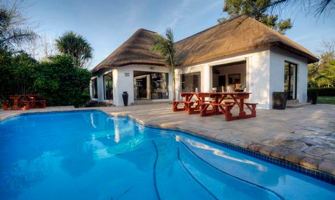 Ein einladendes Gästehaus mit Strohdach, umgeben von üppigem Grün und einem glitzernden Pool im Vordergrund.