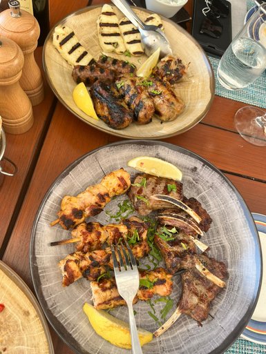 Zwei Teller mit gegrilltem Fleisch, darunter Lammkoteletts und Spieße, garniert mit Zitronenscheiben und frischen Kräutern.