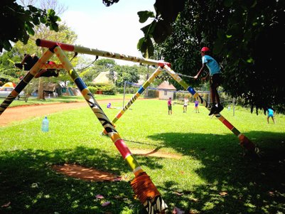 Ein Kind in einem roten Hut klettert auf eine farbenfrohe Spielstruktur im Freien, umgeben von grünem Gras und Bäumen.