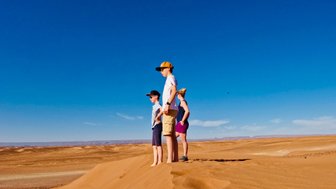 Kinder genießen die Aussicht von einer Dünenkuppe in der Wüste – Familienurlaub in Marokko