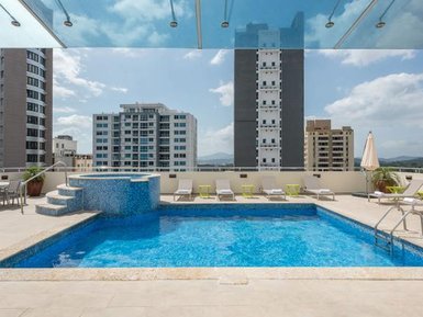 Ein glitzernder Pool auf einer Dachterrasse, umgeben von modernen Gebäuden und einem klaren blauen Himmel.