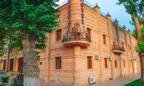 Das Arba Hotel zeigt eine beeindruckende Fassade aus hellen Ziegeln, umgeben von üppigem Grün und einem klaren Himmel.