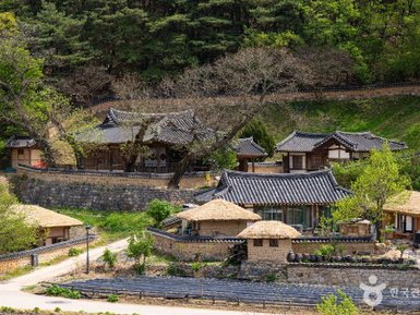 Traditionelle koreanische Häuser mit Reetdächern und Steinmauern, umgeben von üppigem Grün und sanften Hügeln.
