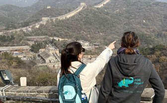 Zwei Frauen stehen auf der Chinesischen Mauer und zeigen auf die beeindruckende Landschaft und die Berge im Hintergrund.