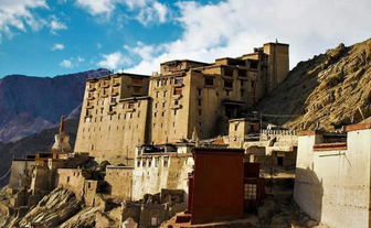 Eine beeindruckende Klosteranlage thront majestätisch auf einem Hügel, umgeben von schroffen Bergen und blauem Himmel.