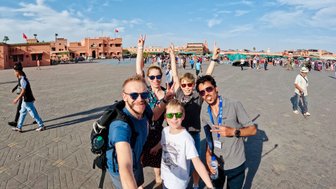 Familie und Guide halten einen gemeinsamen Moment mit einem Selfie auf Djemaa el Fna Platz in Marrakesch fest – Marokko Reise mit Kindern